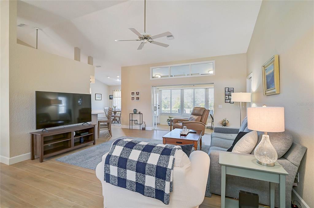 A living room features a vaulted ceiling, a ceiling fan, and a view into a sunroom — 426 BERMUDA ISLES CIRCLE, VENICE, FL