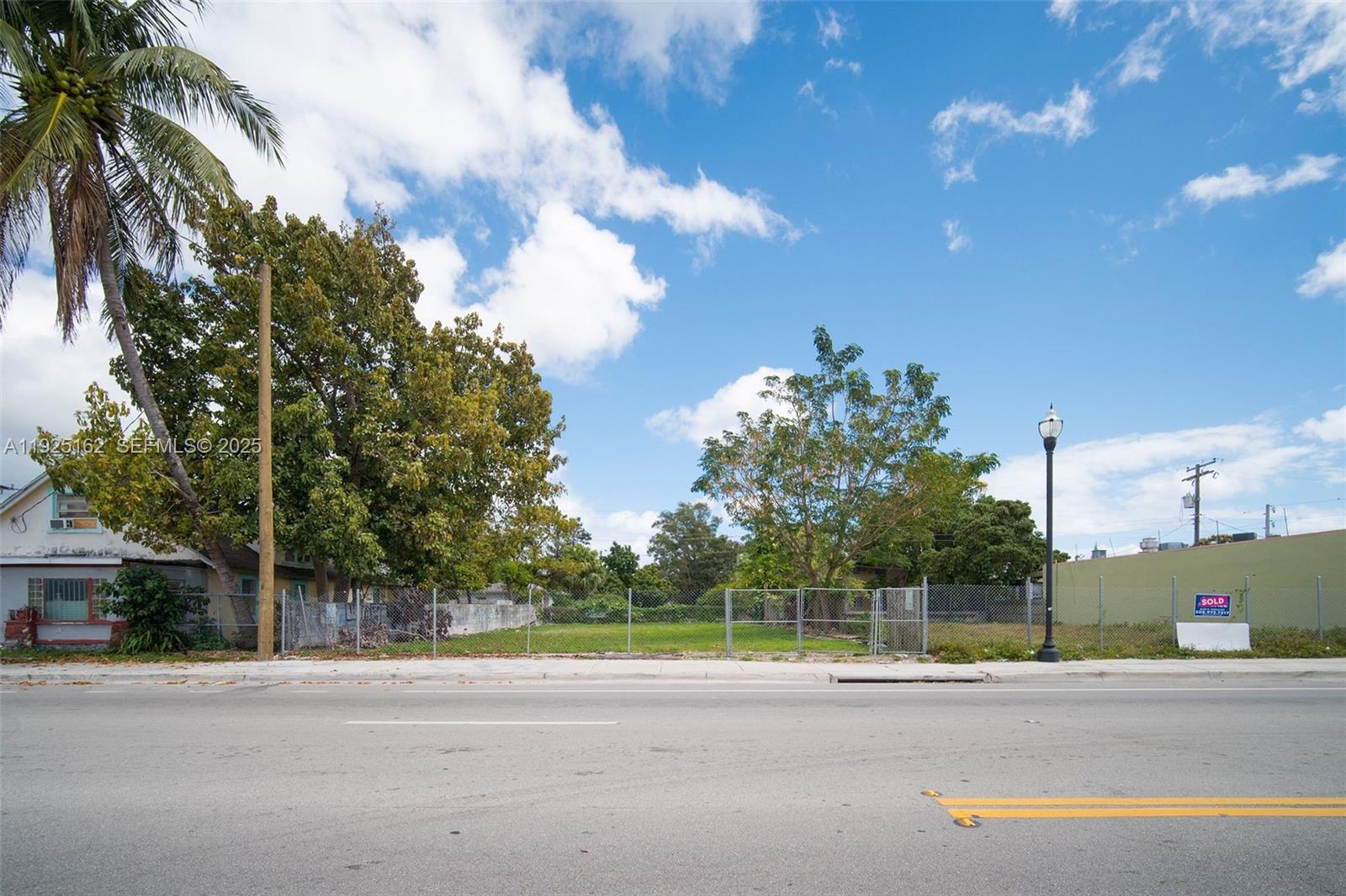 A vacant, fenced-in lot sits between a house and a building along a paved road — 7635 NE 2nd Ave, Miami FL 33138, MIAMI, FL