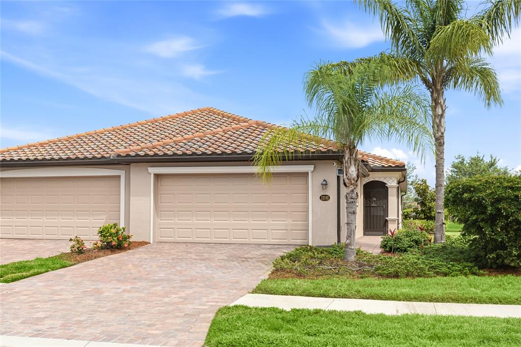 A beige house with a tiled roof, two garage doors, and a palm tree — 12192 AMICA LOOP, VENICE, FL