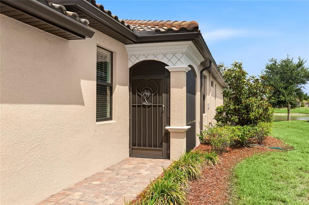 A paved walkway leads to a covered entryway with a decorative screen door and stucco — 12192 AMICA LOOP, VENICE, FL