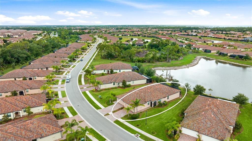 An aerial view shows a suburban house with a tiled roof next to a pond — 12192 AMICA LOOP, VENICE, FL
