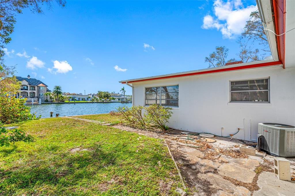 The exterior of a white house features a stone patio, an air conditioning unit, and waterfront views — 5412 PALI WAY, ST PETE BEACH, FL