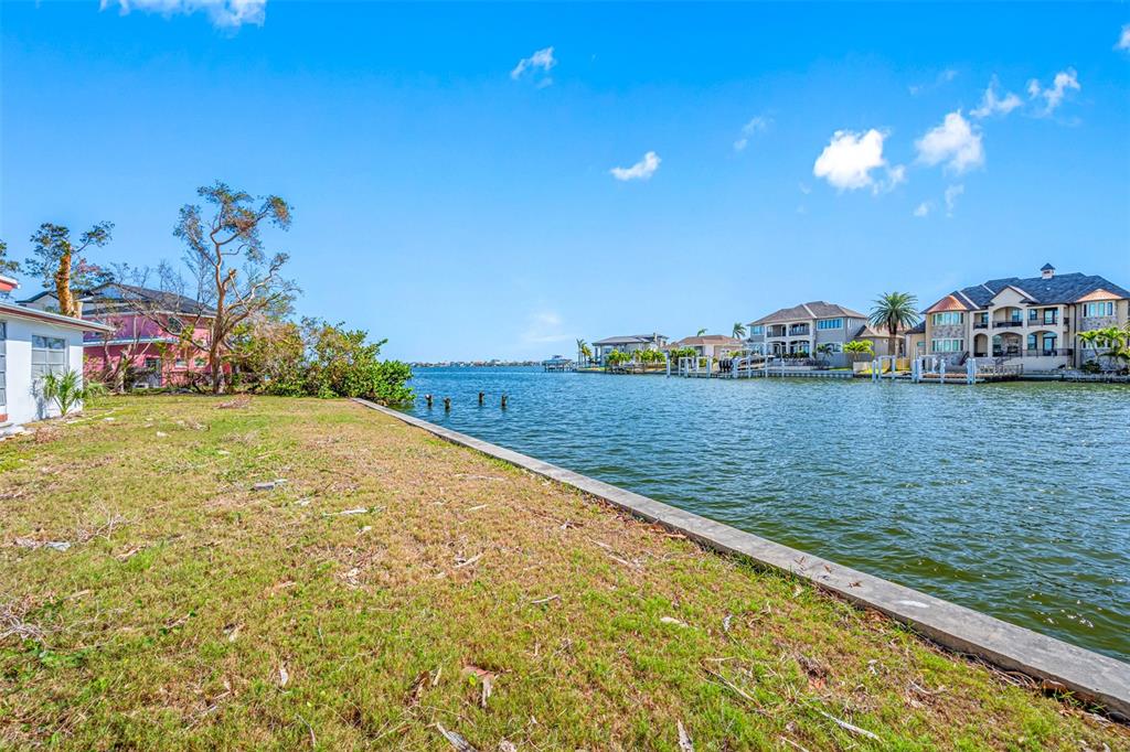 A grassy waterfront lot features a concrete seawall overlooking a canal with neighboring houses — 5412 PALI WAY, ST PETE BEACH, FL
