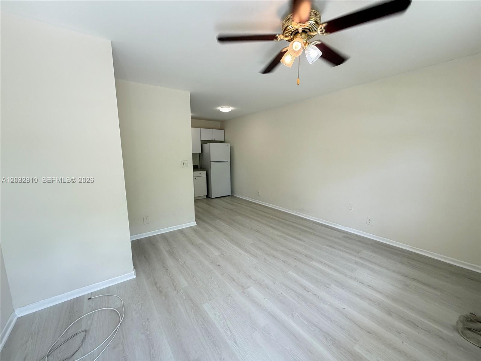 An empty room features light wood-look flooring, a ceiling fan, and a small kitchen area — 4801 SW 18th St # 2, West Park FL 33023, WEST PARK, FL