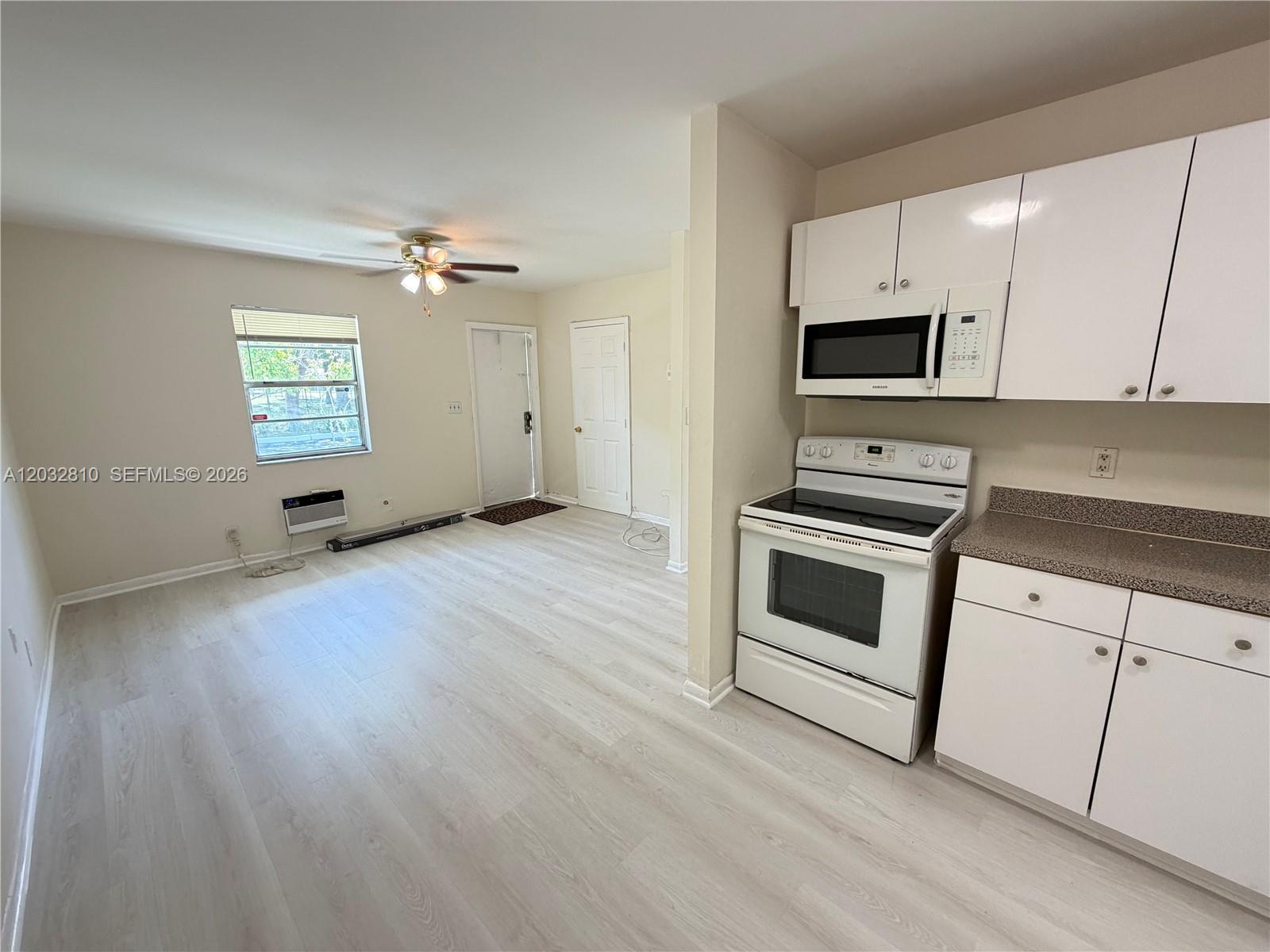 A kitchen with white cabinets and appliances opens into a living area with light flooring — 4801 SW 18th St # 2, West Park FL 33023, WEST PARK, FL
