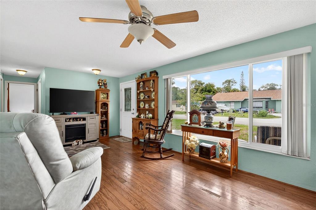 A living room features light blue walls, wood flooring, a ceiling fan, and a large window — 201 POINCIANA AVENUE, PORT ORANGE, FL