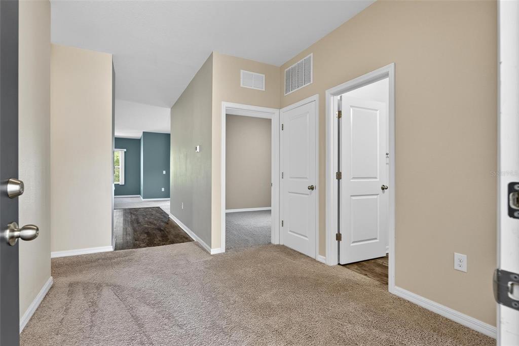 An interior view of a carpeted entryway featuring two white doors and a hallway — 2854 NEVERLAND DRIVE, NEW SMYRNA BEACH, FL