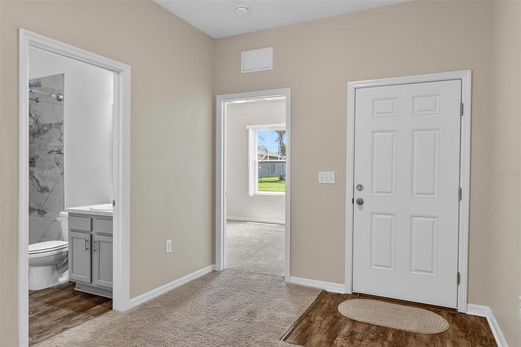 A hallway with beige walls, carpeted flooring, a bathroom, a bedroom doorway, and an entry door — 2854 NEVERLAND DRIVE, NEW SMYRNA BEACH, FL