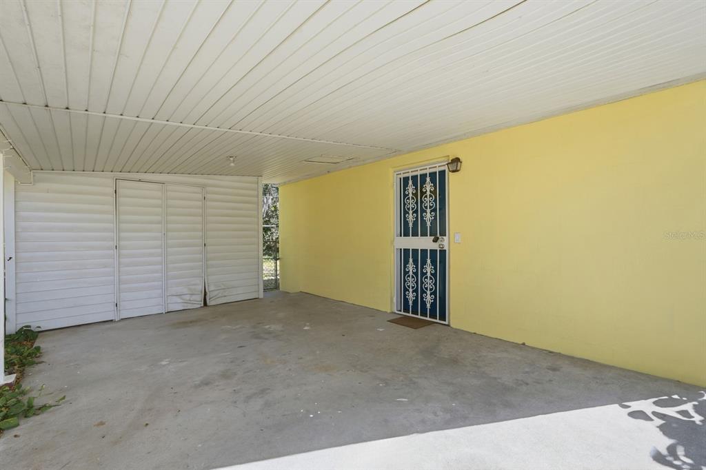 A covered concrete carport features a yellow wall, a decorative metal security door, and siding — 437 LOCKHART STREET, DAYTONA BEACH, FL