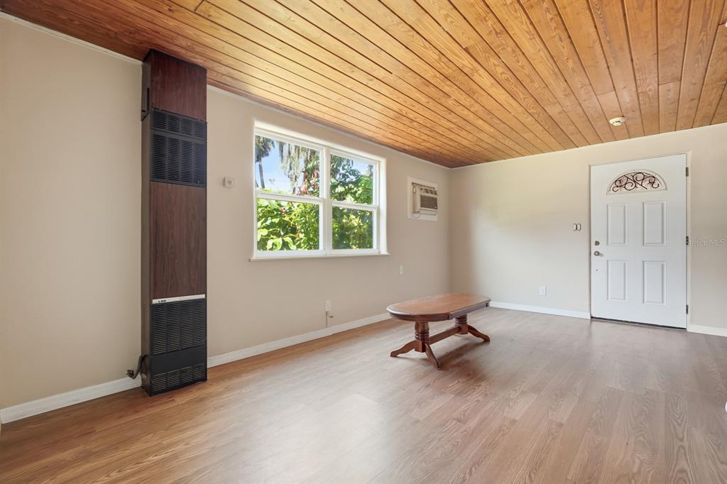 A living room features wood-paneled ceilings, light-colored walls, wood-look flooring, a wall heater, and a door — 437 LOCKHART STREET, DAYTONA BEACH, FL
