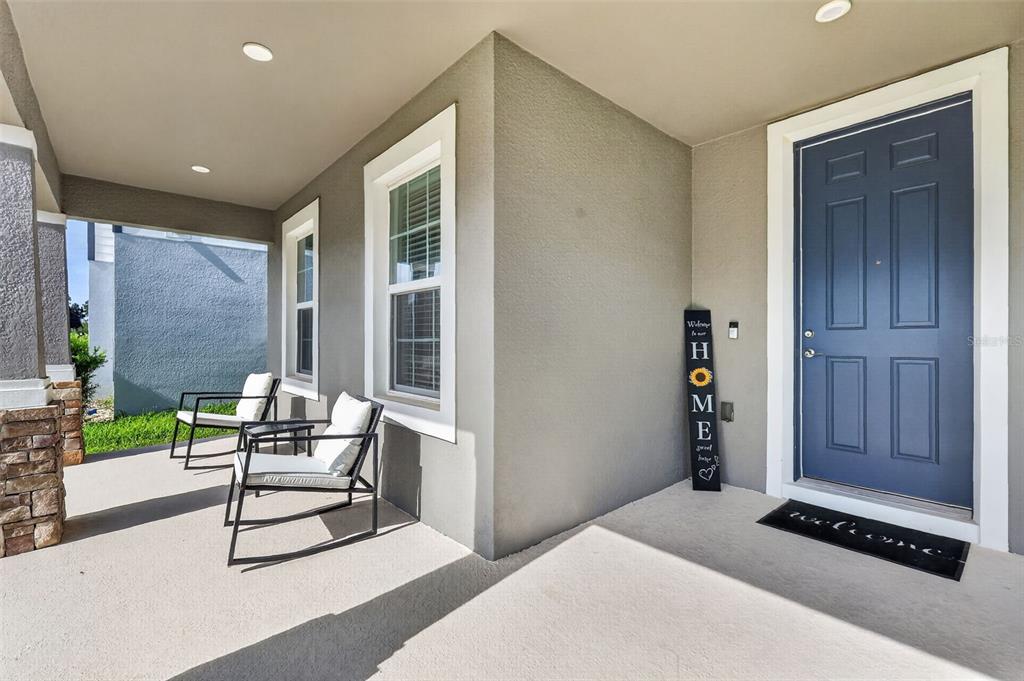 A covered front porch features two chairs, a blue door, and a vertical welcome sign — 3859 DENALI DR, APOPKA, FL