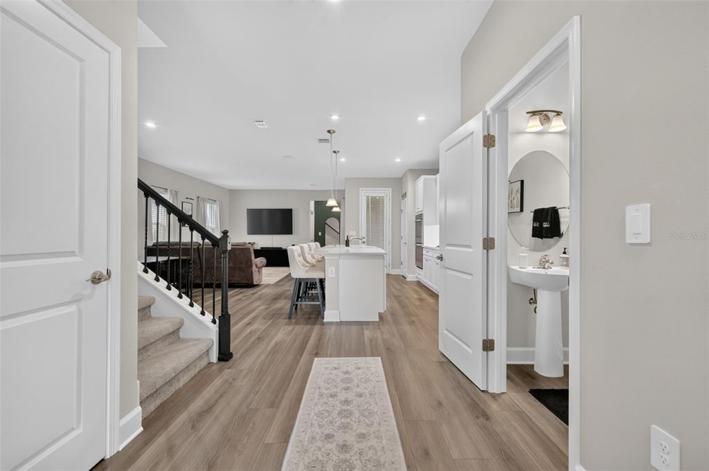 A hallway leads to an open-concept kitchen and living area with wood-look flooring — 3859 DENALI DR, APOPKA, FL