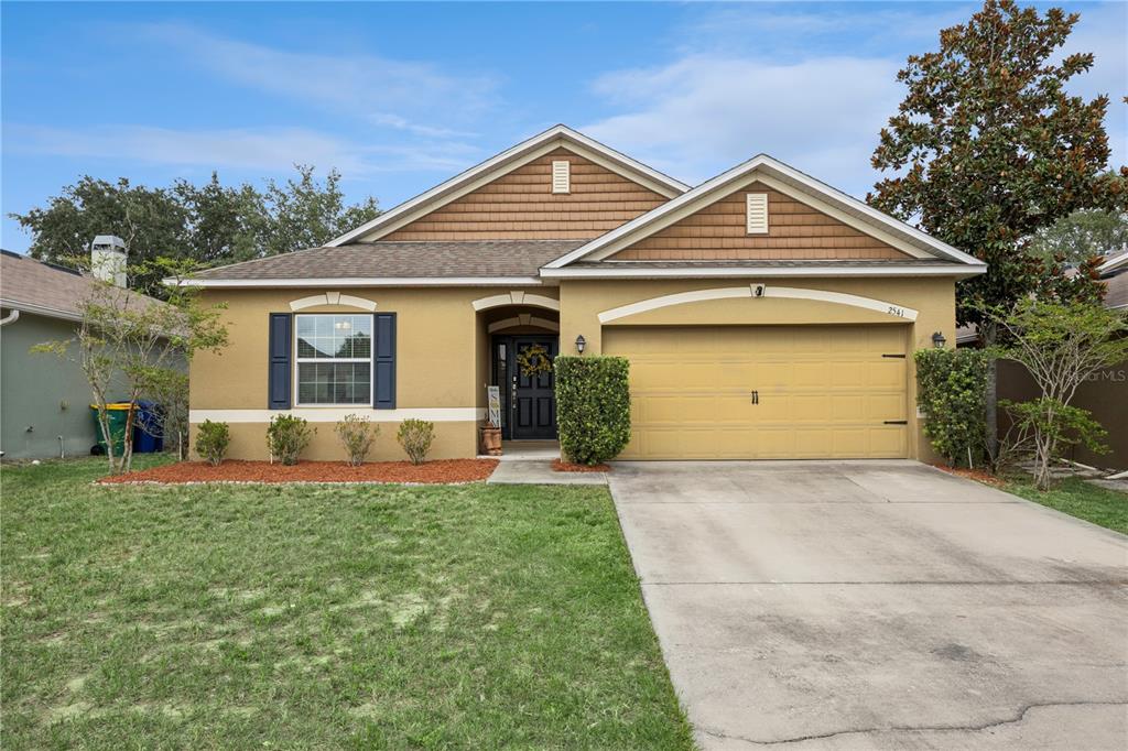 A single-story house with a tan stucco exterior, brown shingle roof, and a two-car garage — 2541 MARTINS RUN, TAVARES, FL