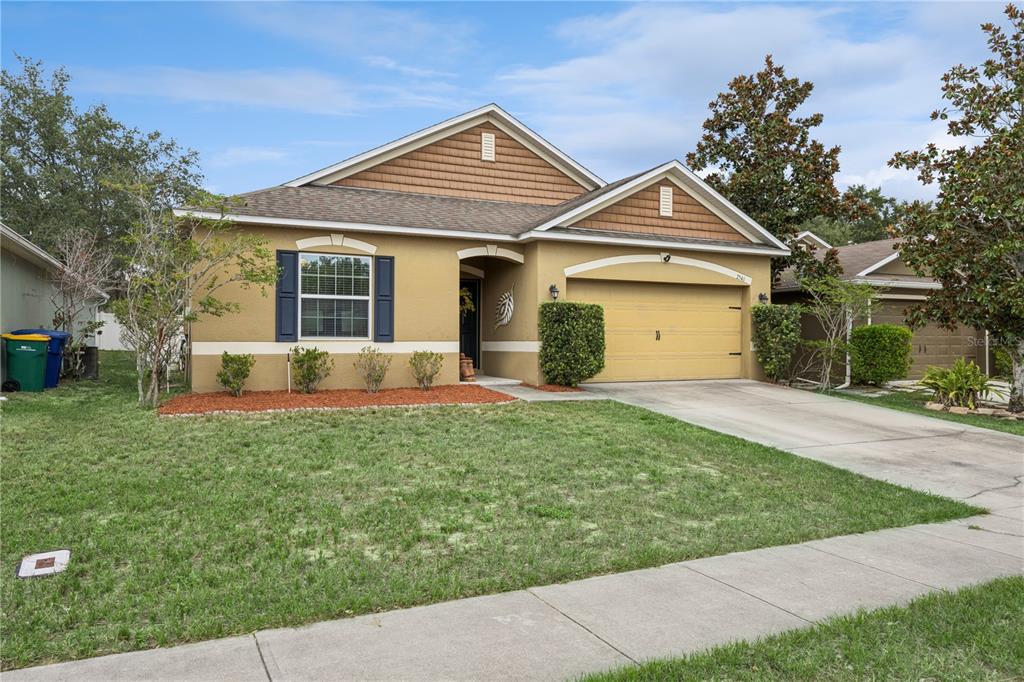 A single-story house with a tan stucco exterior, brown shingle roof, and a two-car garage — 2541 MARTINS RUN, TAVARES, FL