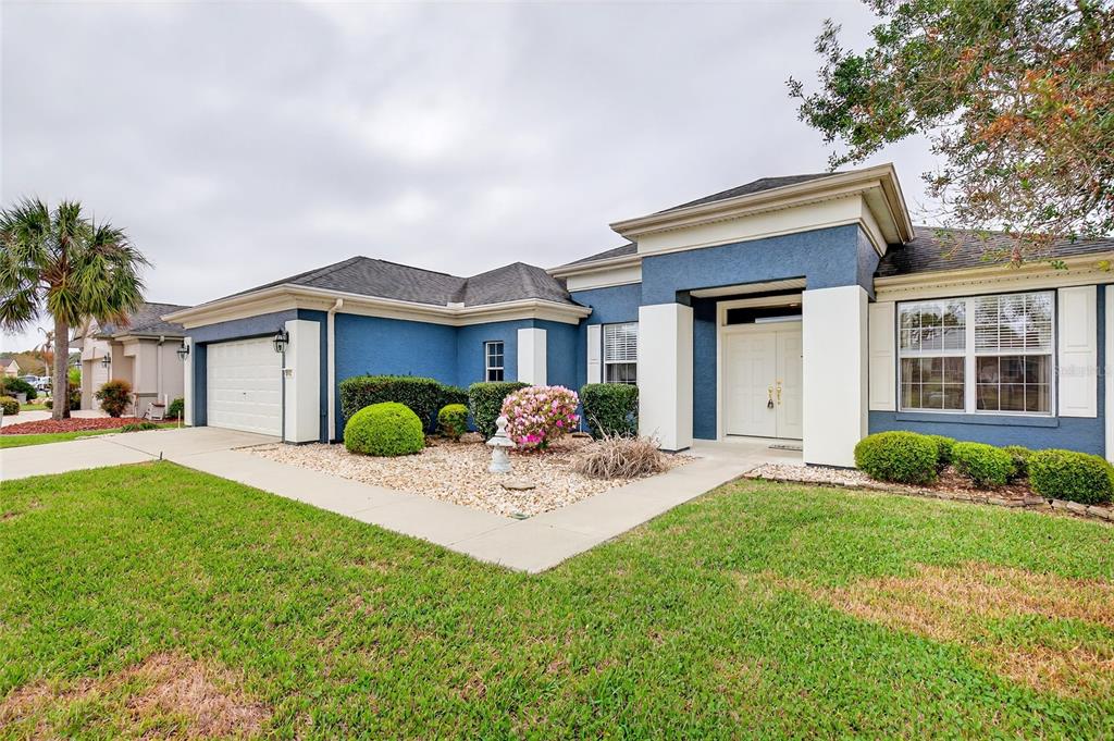 A blue single-story house with a white garage, white trim, and a landscaped front yard — 8842 SE 118TH LANE, SUMMERFIELD, FL
