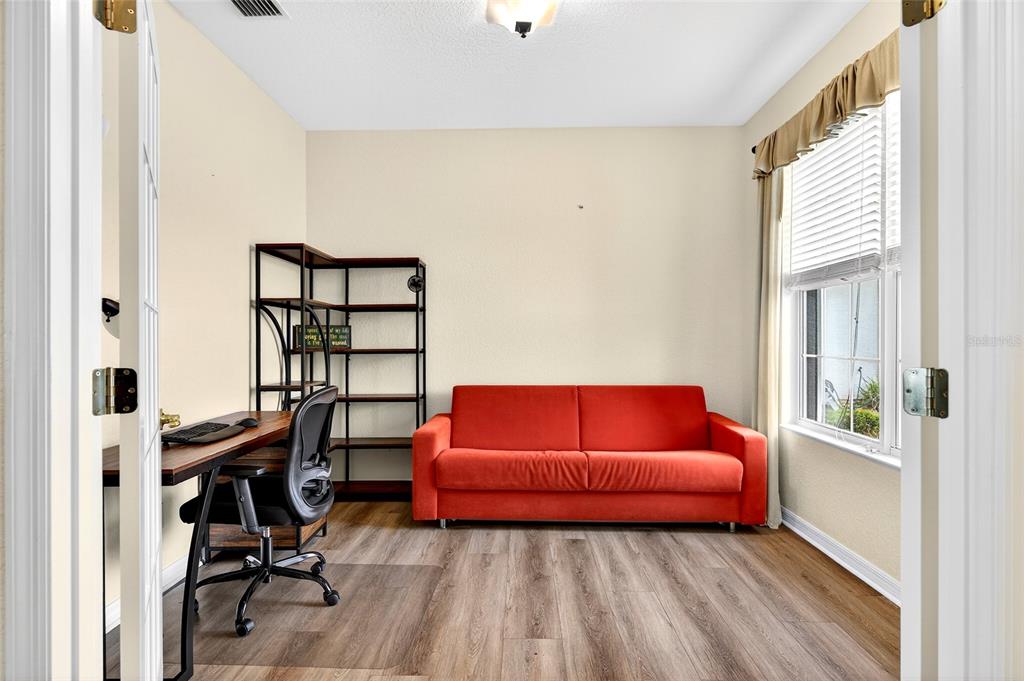 A home office features a red sofa, a desk with a chair, and wood-look flooring — 8842 SE 118TH LANE, SUMMERFIELD, FL