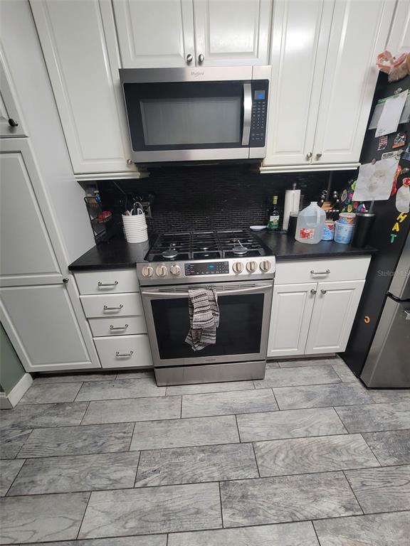 A kitchen features white cabinets, stainless steel appliances, a gas range, and gray wood-look flooring — 617 SAILBOAT DRIVE, NICEVILLE, FL