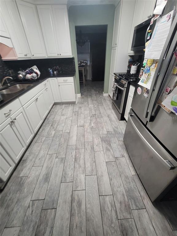 A kitchen features white cabinets, black countertops, stainless steel appliances, and gray wood-look flooring — 617 SAILBOAT DRIVE, NICEVILLE, FL