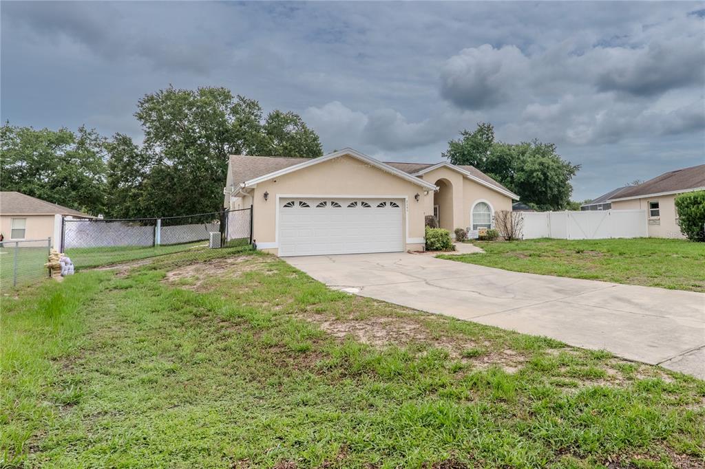 A single-story house with a white garage door and a concrete driveway under a cloudy sky — 7444 PARADISE COVE PLACE, LAKELAND, FL