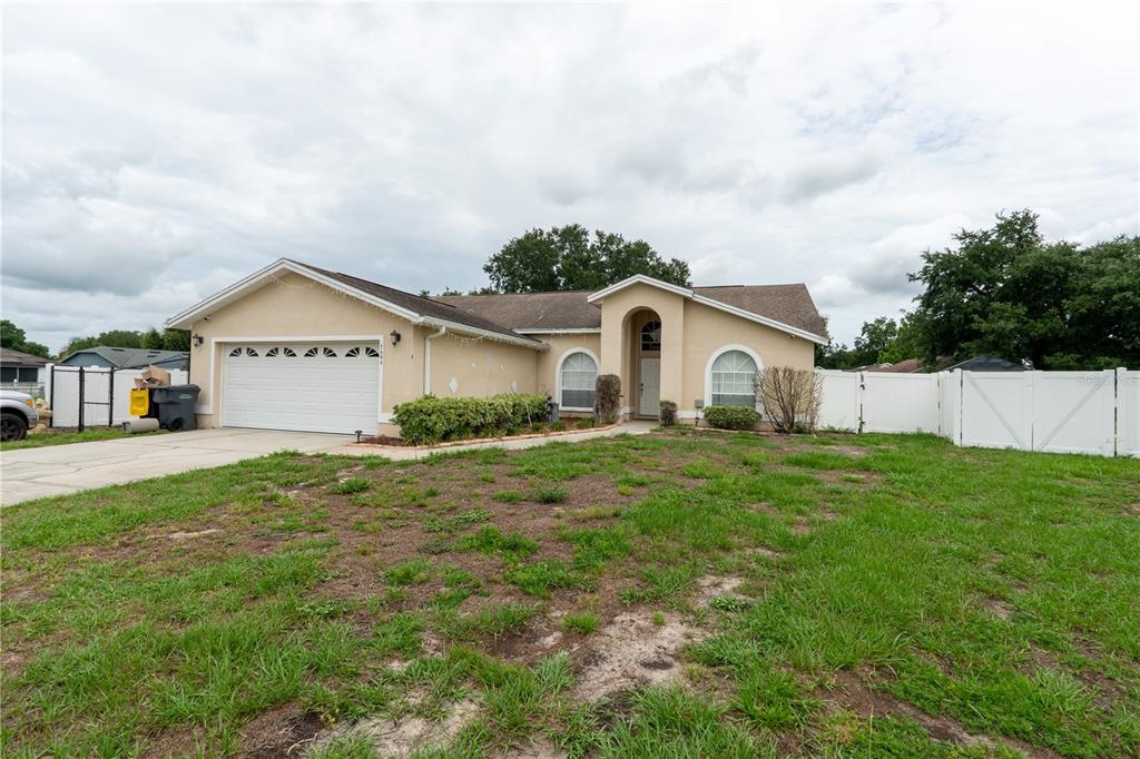 A single-story house with a beige stucco exterior, a two-car garage, and a white fence — 7444 PARADISE COVE PLACE, LAKELAND, FL