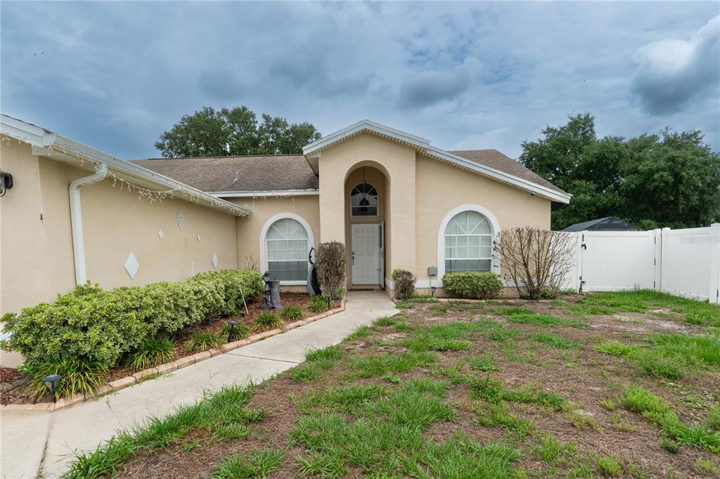 A single-story tan house with an arched entryway and a concrete walkway leading to the door — 7444 PARADISE COVE PLACE, LAKELAND, FL