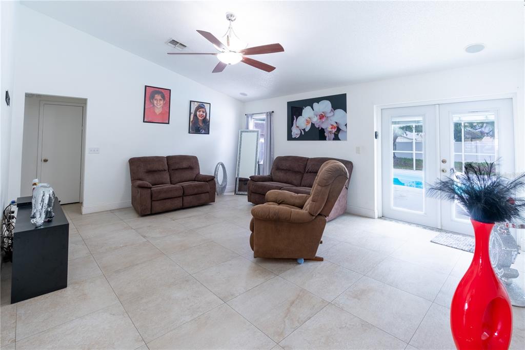 A living room features tile flooring, brown furniture, a ceiling fan, and glass patio doors — 7444 PARADISE COVE PLACE, LAKELAND, FL