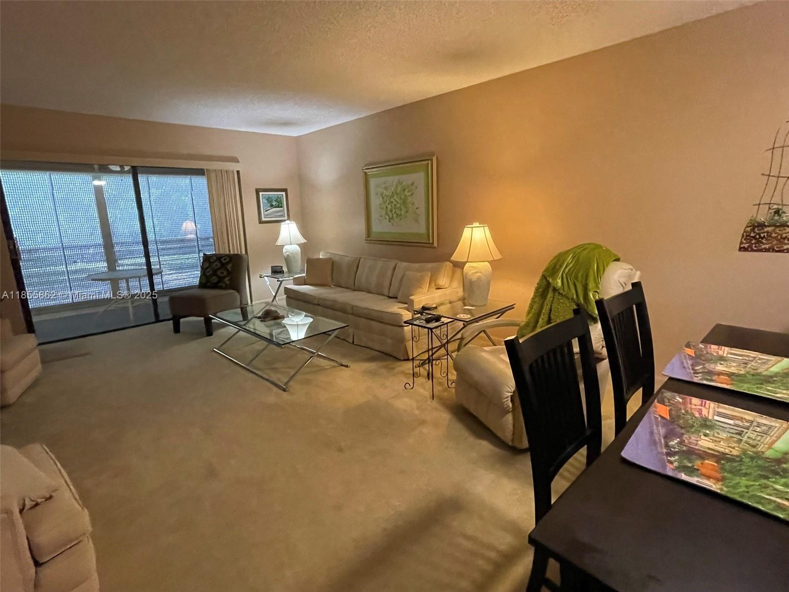 A living room features beige carpeting, a sofa, a glass coffee table, and a dining set — 4975 E Sabal Palm Blvd # 208, Tamarac FL 33319, TAMARAC, FL