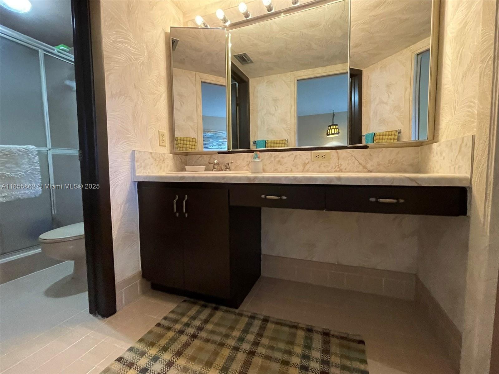 A bathroom features a dark wood vanity with a marble countertop and a tri-fold mirror — 4975 E Sabal Palm Blvd # 208, Tamarac FL 33319, TAMARAC, FL