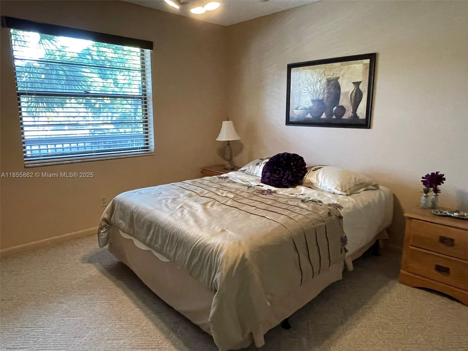 A bedroom features a bed with a tan comforter, a window, and a wall painting — 4975 E Sabal Palm Blvd # 208, Tamarac FL 33319, TAMARAC, FL