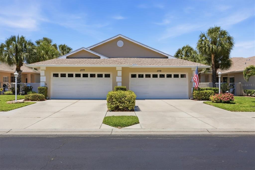 A duplex house with two garage doors and a shared driveway under a blue sky — 1777 FOUNTAIN VIEW CIRCLE, VENICE, FL