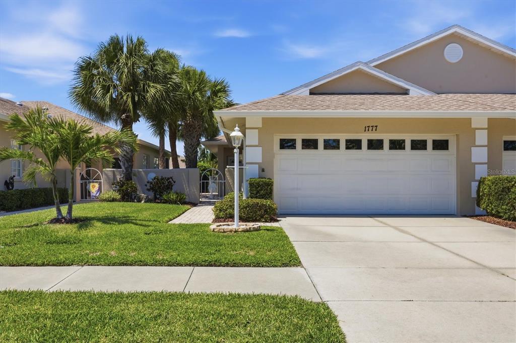 A beige single-story house with a white garage door, palm trees, and a paved walkway — 1777 FOUNTAIN VIEW CIRCLE, VENICE, FL