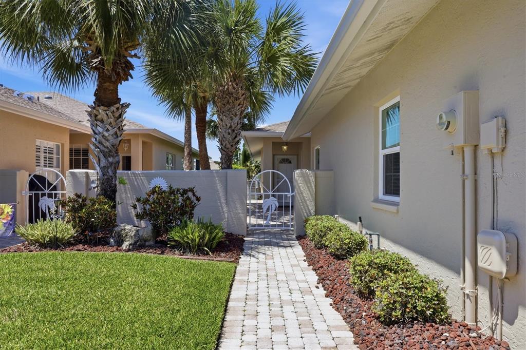 A paved walkway leads to a gated courtyard entrance beside a house with palm trees — 1777 FOUNTAIN VIEW CIRCLE, VENICE, FL