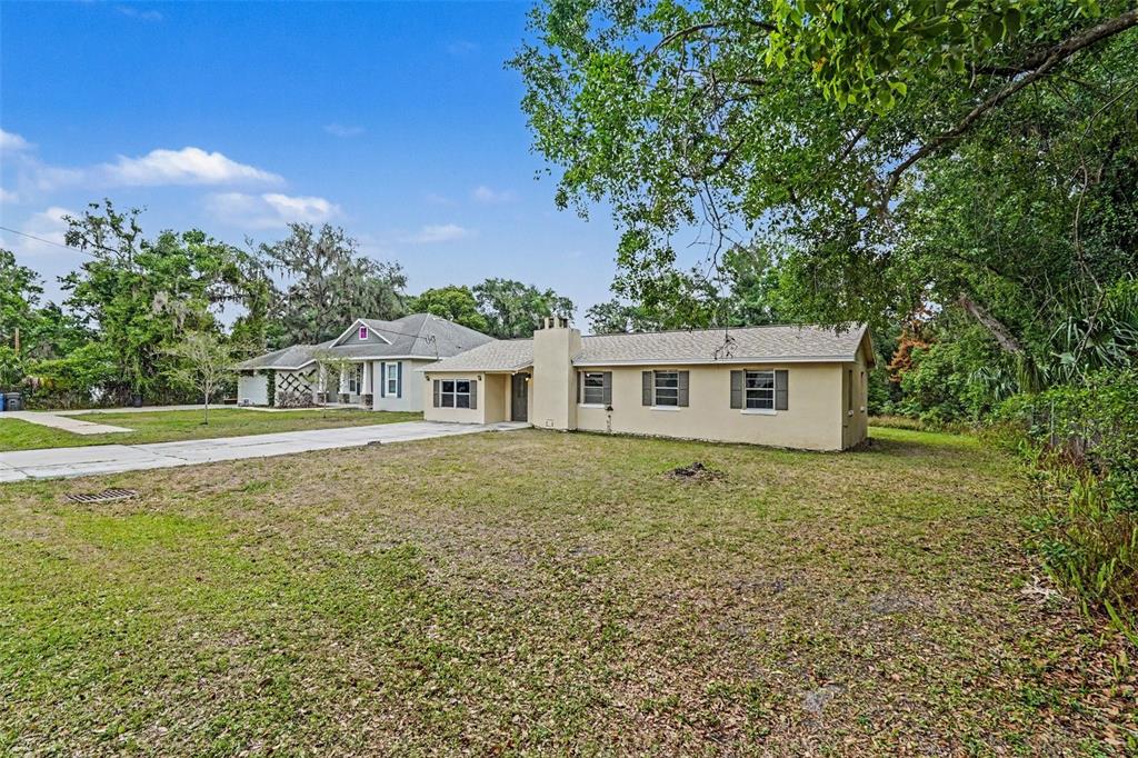 A tan, single-story house with a chimney stands on a grassy lot near trees — 7206 ALAFIA DRIVE, RIVERVIEW, FL