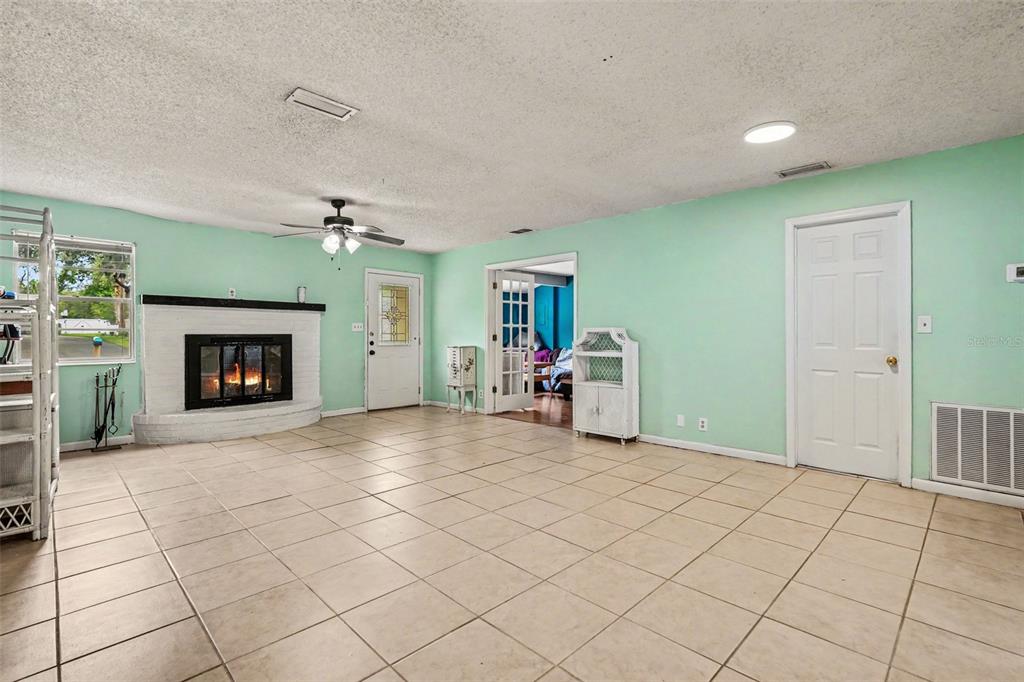 A living room with light green walls, tile flooring, a white brick fireplace, and ceiling fan — 7206 ALAFIA DRIVE, RIVERVIEW, FL