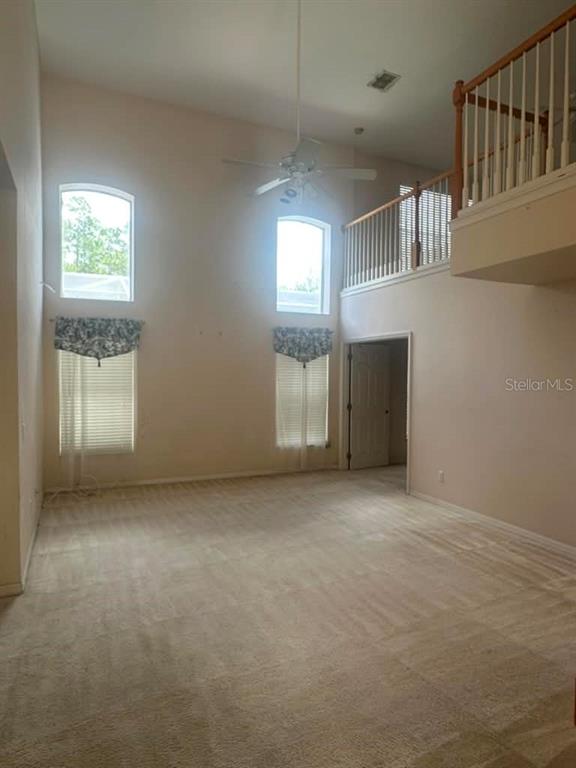 A high-ceilinged living room features beige carpet, two windows with valances, and a loft railing — 948 TROON CIRCLE, DAVENPORT, FL