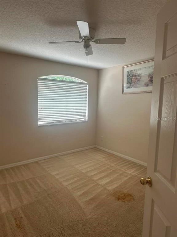 An empty bedroom features beige carpet, a ceiling fan, and a window with blinds — 948 TROON CIRCLE, DAVENPORT, FL