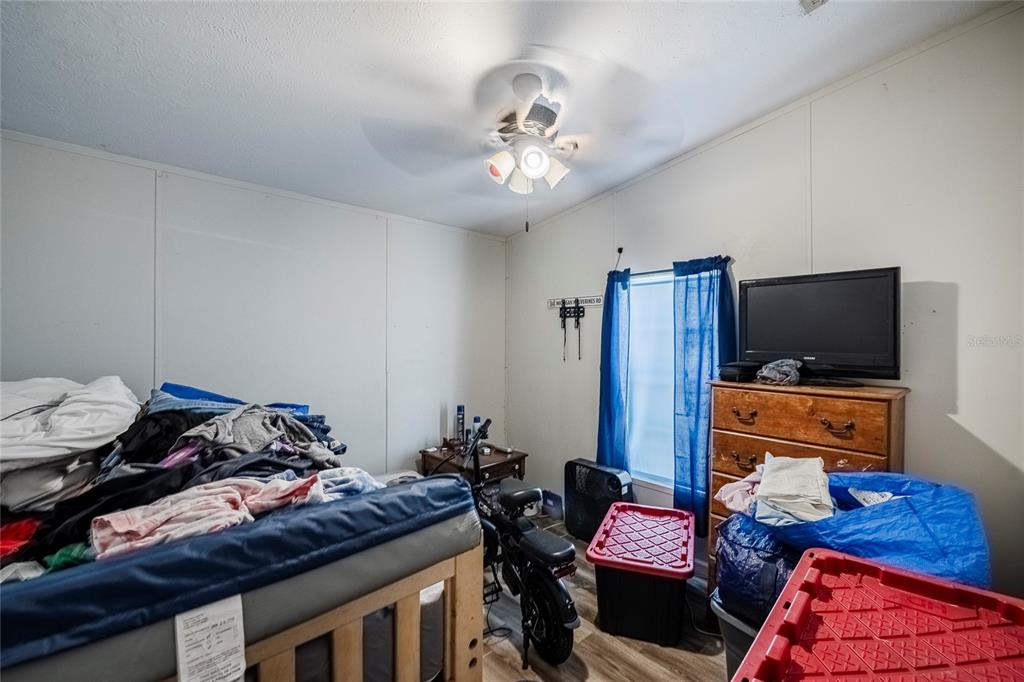 A bedroom with a ceiling fan, a wooden dresser with a television, and cluttered furniture — 3825 CARRIAGE DRIVE, LAKE WALES, FL