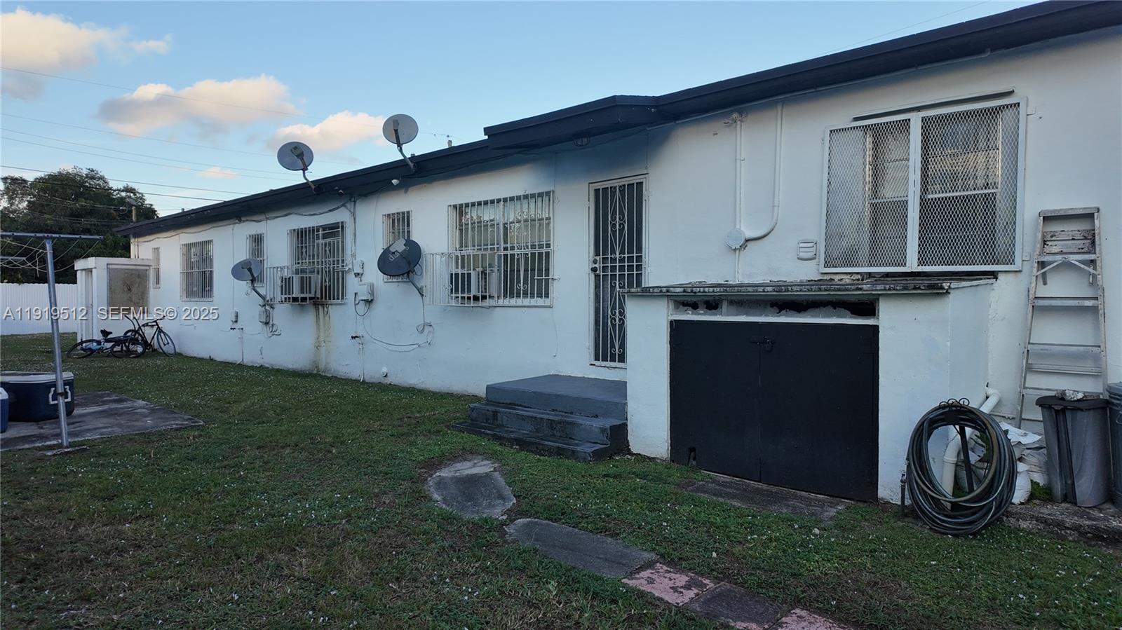 The exterior of a white, single-story building features multiple windows with security bars and satellite dishes — 9700 NW 20th Ave, Miami FL 33147, MIAMI, FL