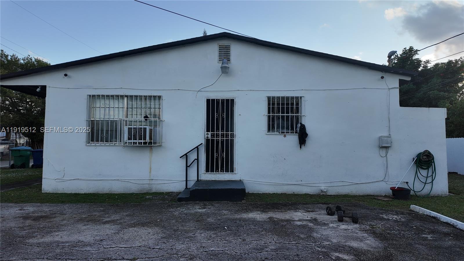 The exterior of a white, single-story house features a central door and two barred windows — 9700 NW 20th Ave, Miami FL 33147, MIAMI, FL
