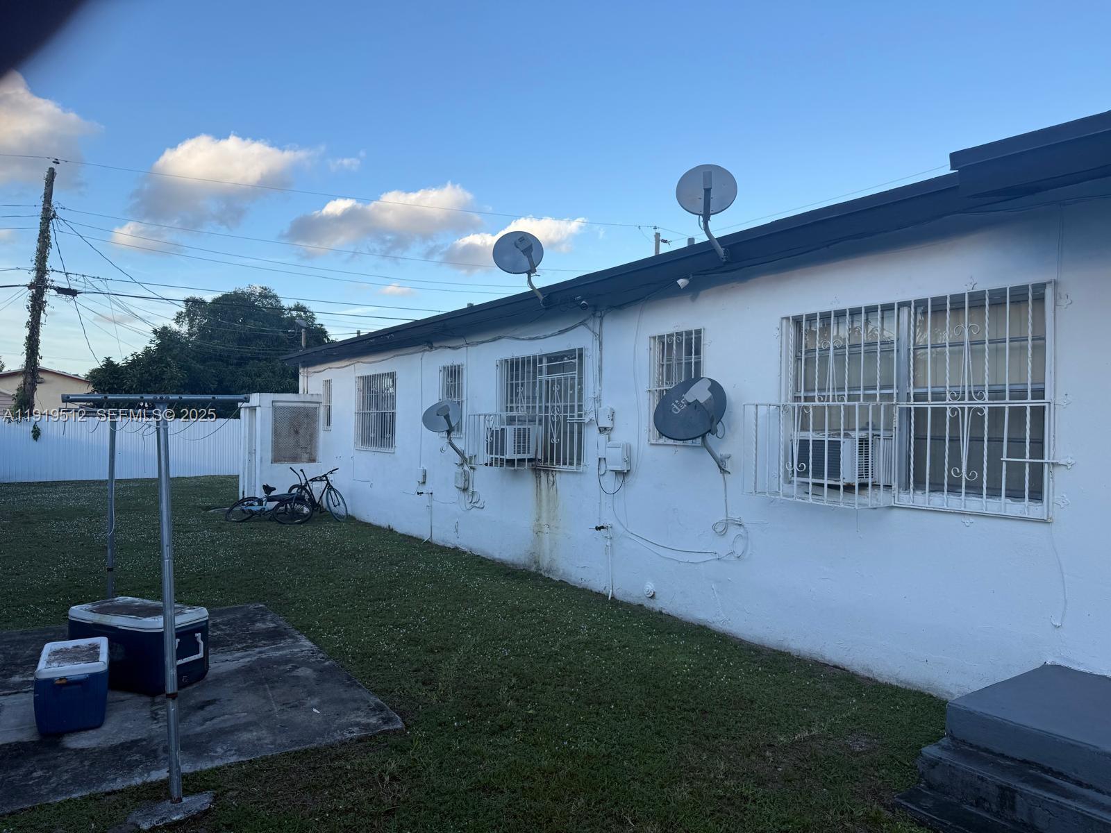 The exterior of a white house features multiple satellite dishes, window security bars, and air conditioners — 9700 NW 20th Ave, Miami FL 33147, MIAMI, FL