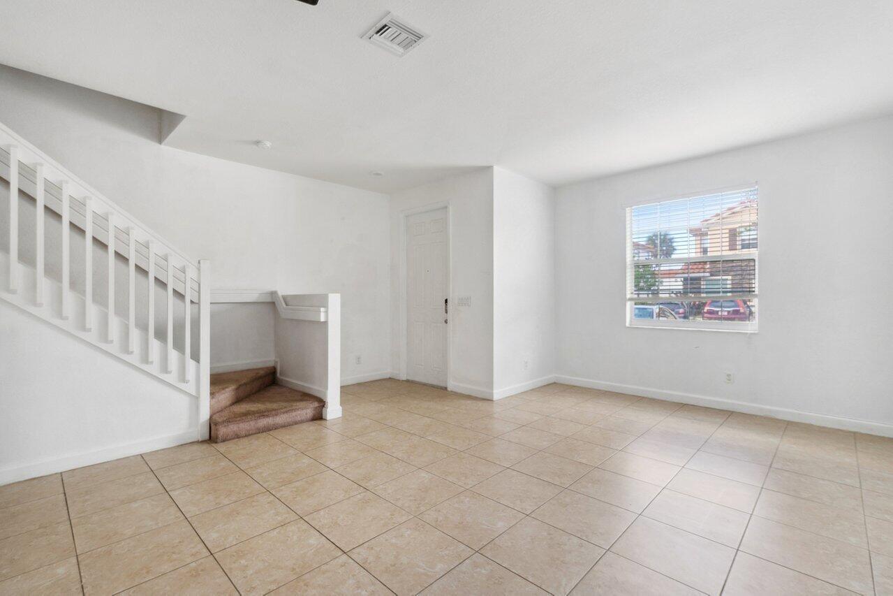 An empty room with white walls, tile flooring, a staircase, and a window — 5288 Ashley River Road, West Palm Beach FL 33417, WEST PALM BEACH, FL