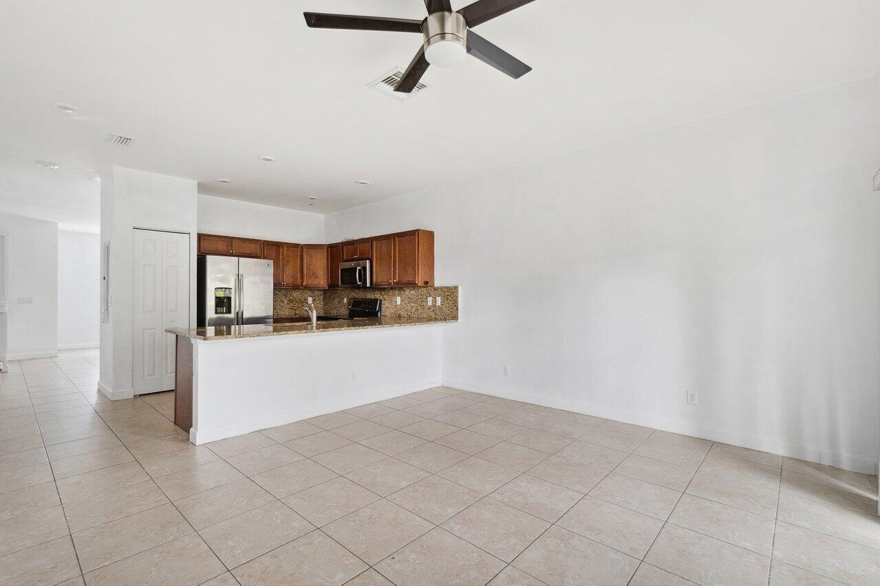 An open-concept kitchen with wood cabinets and granite countertops overlooks a tiled living area — 5288 Ashley River Road, West Palm Beach FL 33417, WEST PALM BEACH, FL