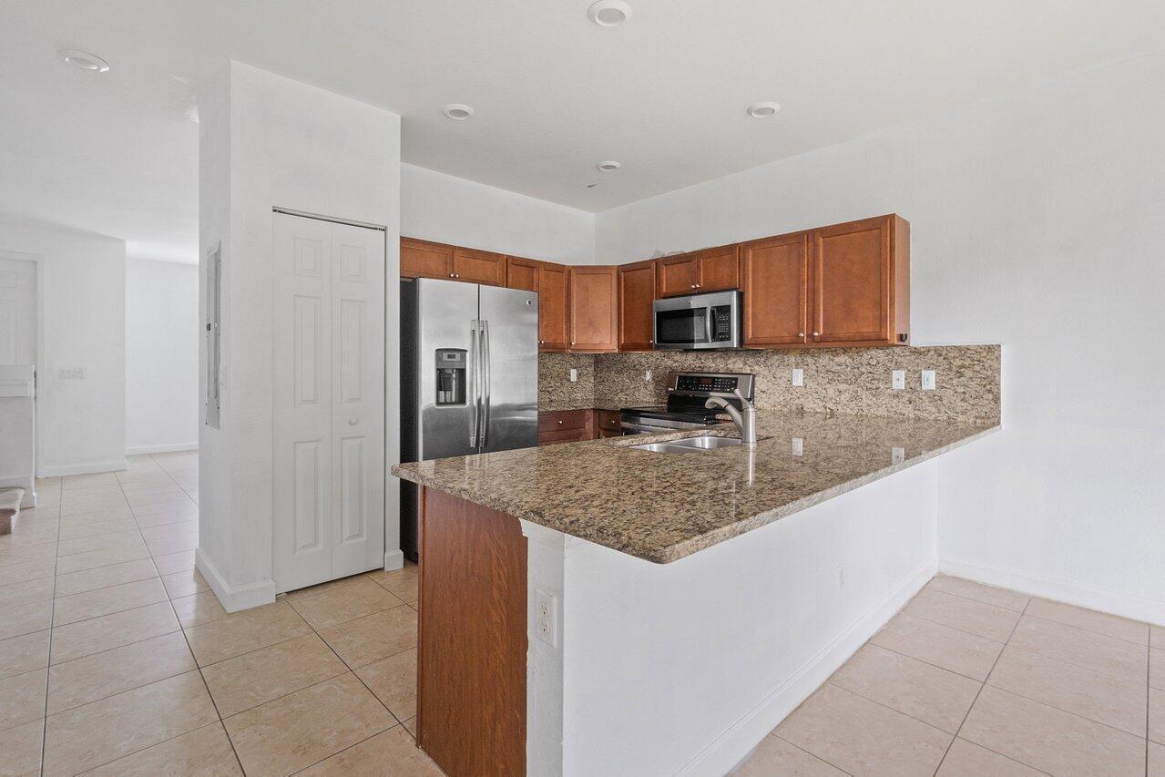 A kitchen with wood cabinets, granite countertops, stainless steel appliances, and tile flooring — 5288 Ashley River Road, West Palm Beach FL 33417, WEST PALM BEACH, FL