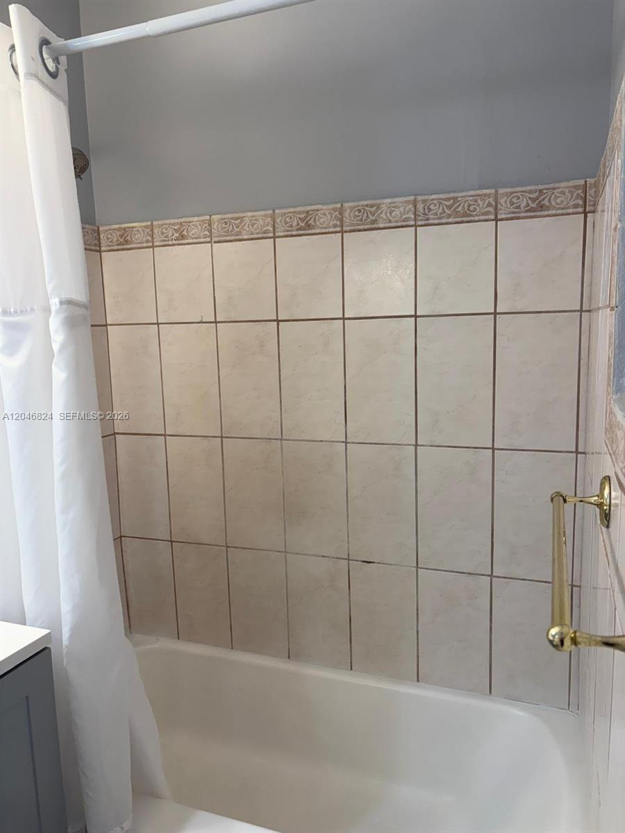 A bathtub with a shower curtain and beige tiled walls featuring a decorative border — 1101 NE 5th St # 1, Hallandale Beach FL 33009, HALLANDALE BEACH, FL