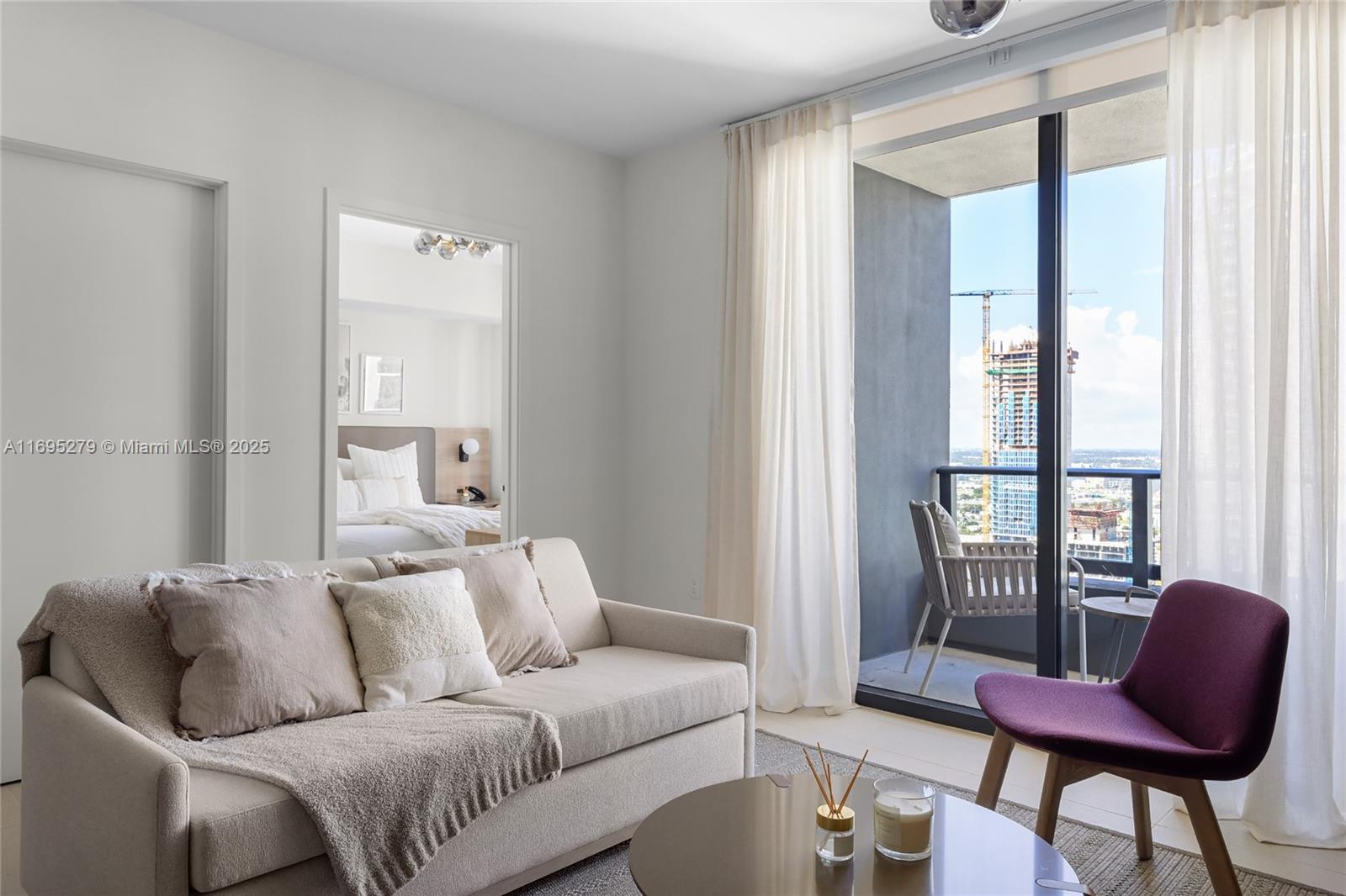 A living room with a beige sofa, purple chair, and balcony overlooking a construction site — 159 NE 6TH ST # 3209, Miami FL 33132, MIAMI, FL