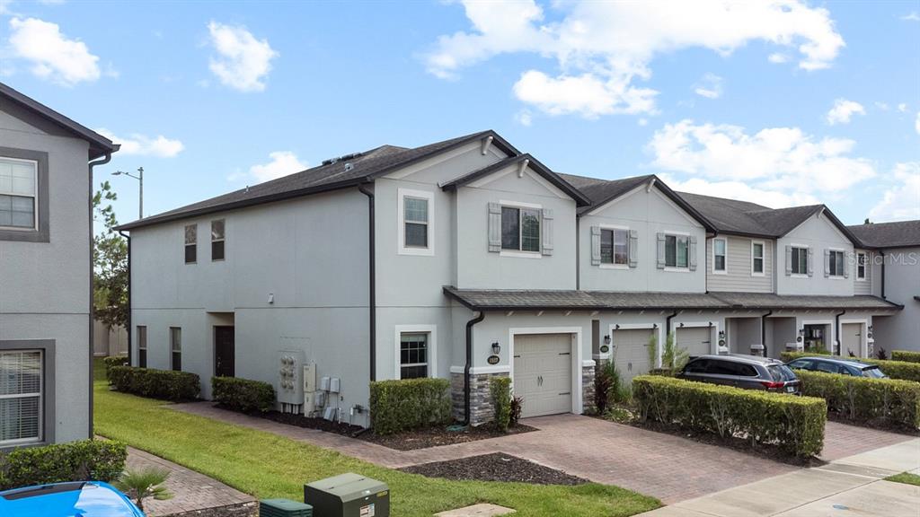 A row of multi-story townhomes with gray stucco siding, stone accents, and attached garages — 1037 FLOWING TIDE DRIVE, ORLANDO, FL