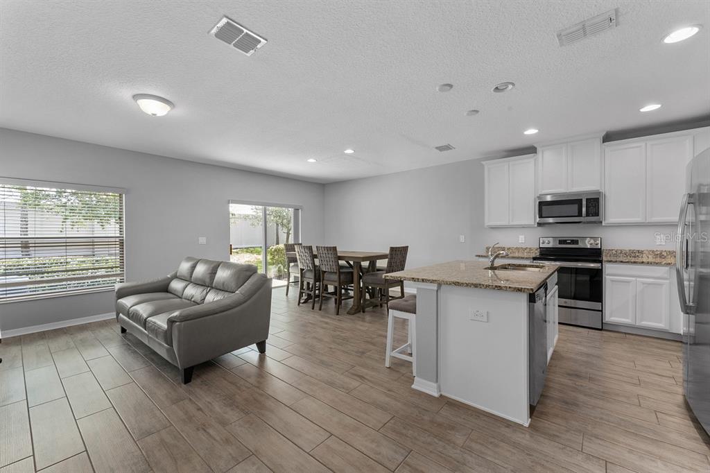 An open-concept kitchen and living area features light wood-look tile floors and white cabinetry — 1037 FLOWING TIDE DRIVE, ORLANDO, FL
