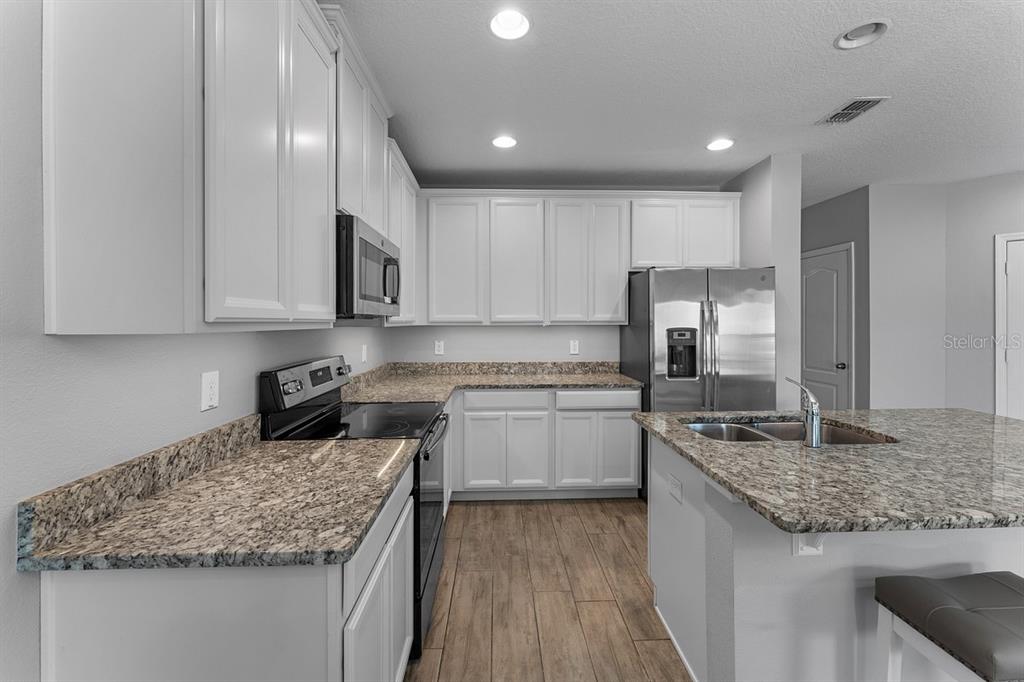 A kitchen features white cabinets, granite countertops, stainless steel appliances, and wood-look tile flooring — 1037 FLOWING TIDE DRIVE, ORLANDO, FL