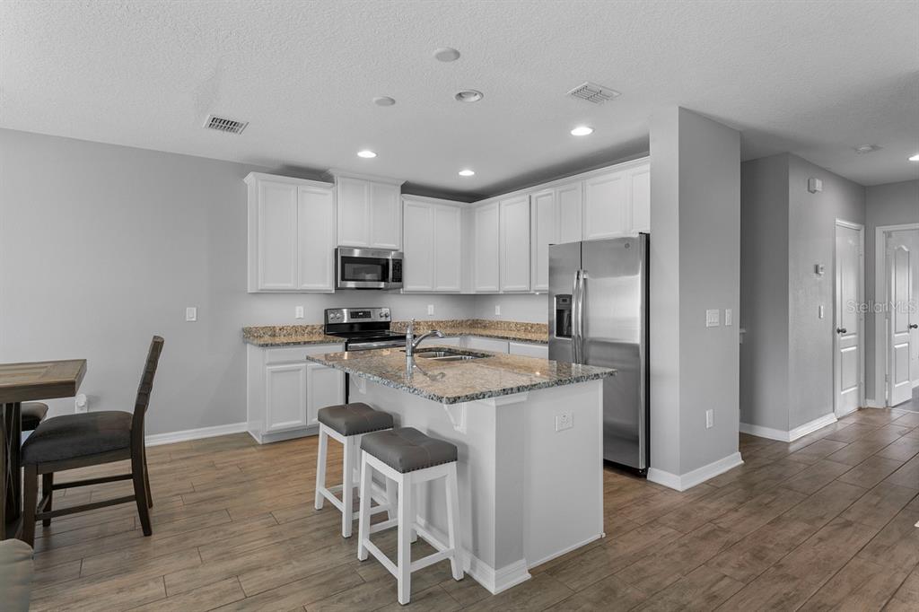 A kitchen features white cabinets, granite countertops, a center island with stools, and stainless appliances — 1037 FLOWING TIDE DRIVE, ORLANDO, FL