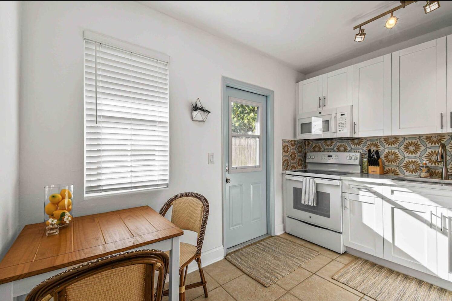 A kitchen features white cabinets, patterned backsplash tiles, a light blue door, and a dining area — 427 Conniston Road # B, West Palm Beach FL 33405, WEST PALM BEACH, FL